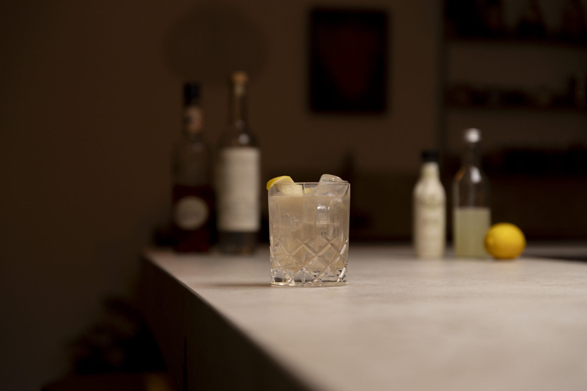 Rhubarb liqueur, mezcal, lemon juice, lemon, celery bitters and sugar syrup laid out on a white bar table