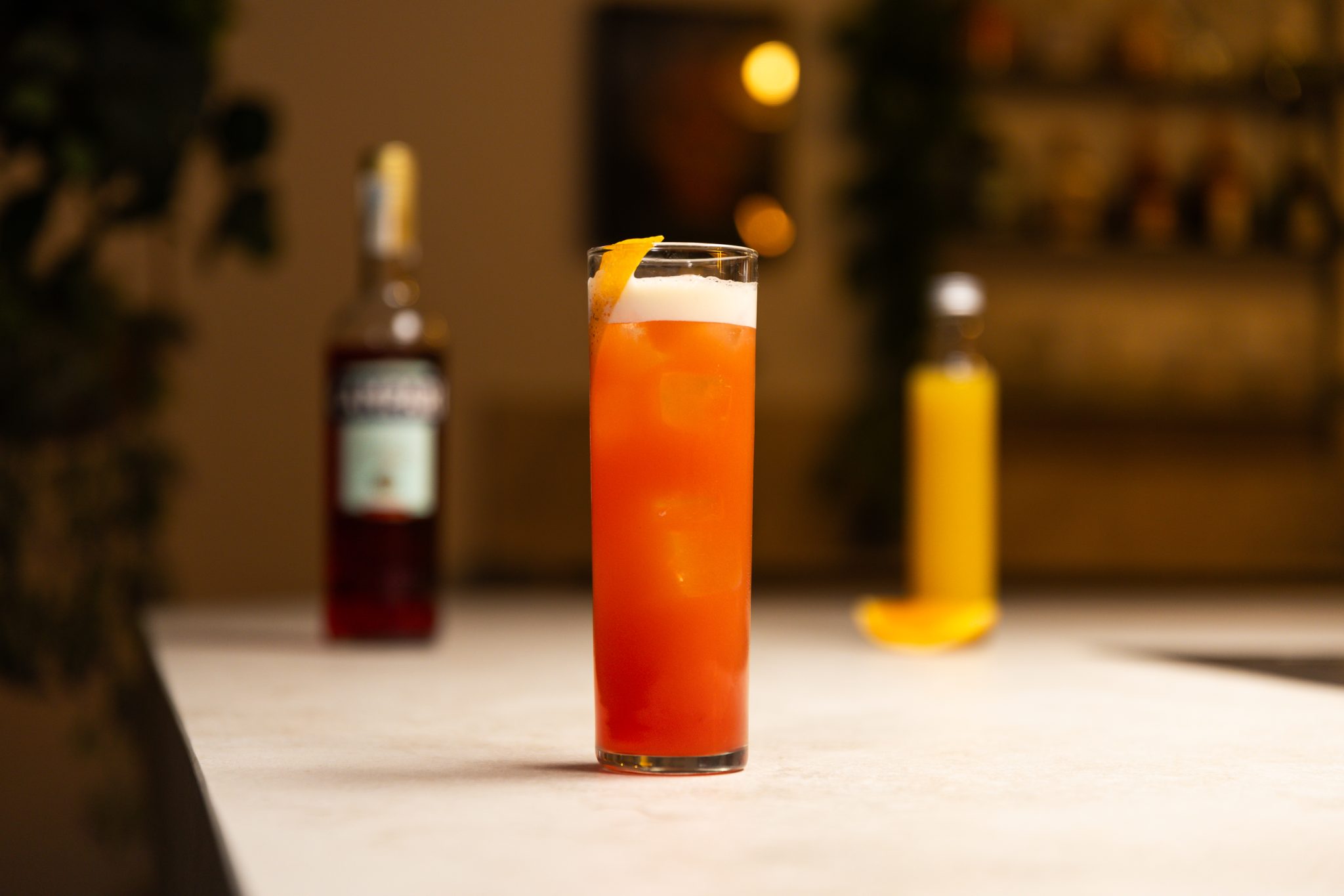 Campari, orange juice and an orange wedge laid out on a white bar table