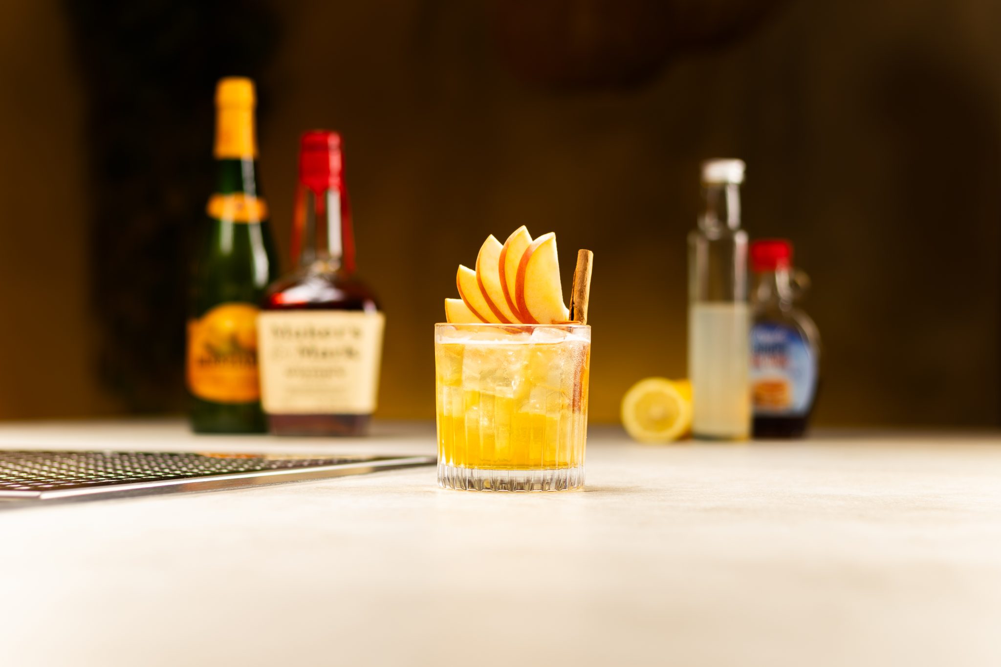 Bourbon, apple cider, lemon juice, two lemons and maple syrup laid out on a white bar table