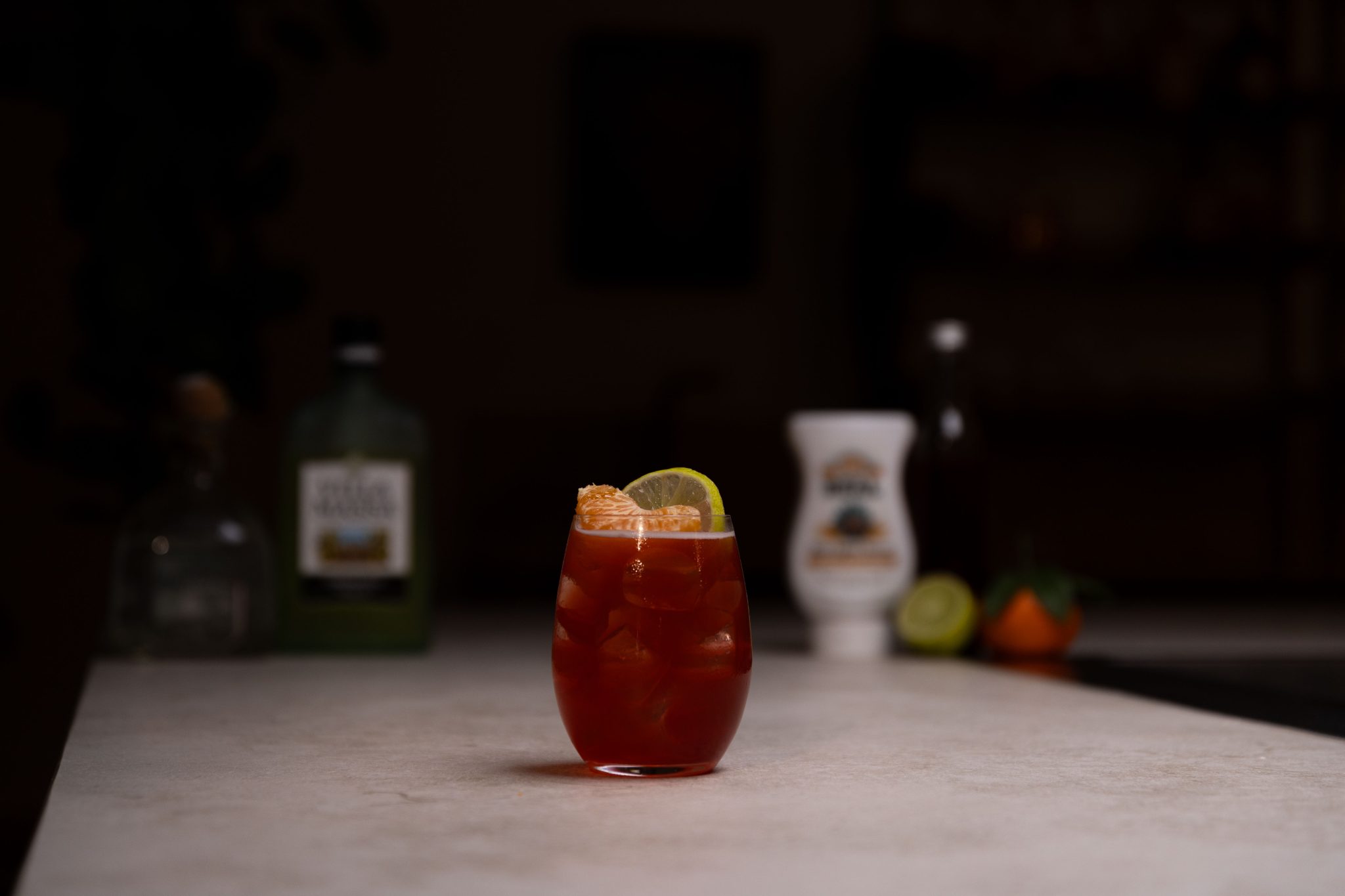 Tequila, limoncello, pomegranate juice, lime juice, lime, tangerine juice and agave syrup laid out on a white bar table