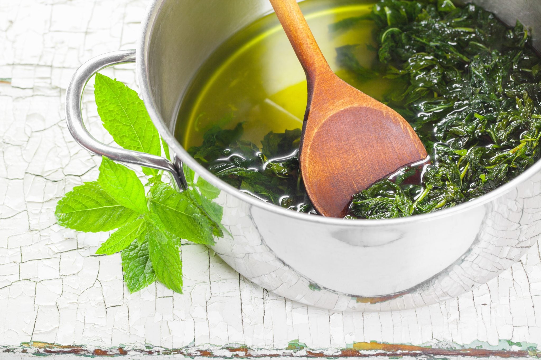 A shot of a pot with homemade mint syrup and a wooden spoon