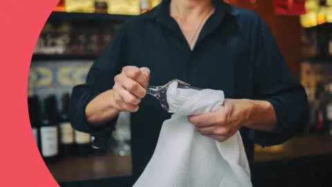 A shot of a Bartender drying a wine glass with a white cloth