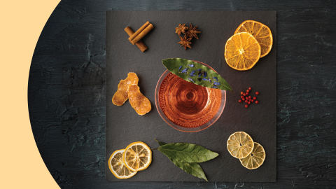 A shot of a square black stone tray from above with three anise stars, two cinnamon sticks, six dehydrated citrus slices, and a cocktail in a martini glass on top