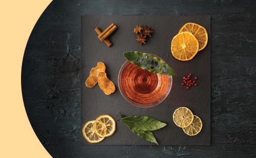 A shot of a square black stone tray from above with three anise stars, two cinnamon sticks, six dehydrated citrus slices, and a cocktail in a martini glass on top