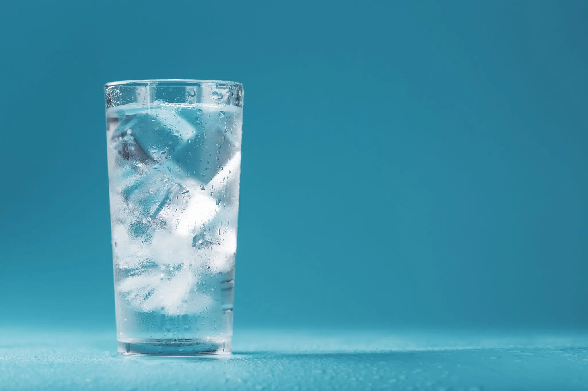 A side shot of a chilled glass filled with ice and water in front of a blue background