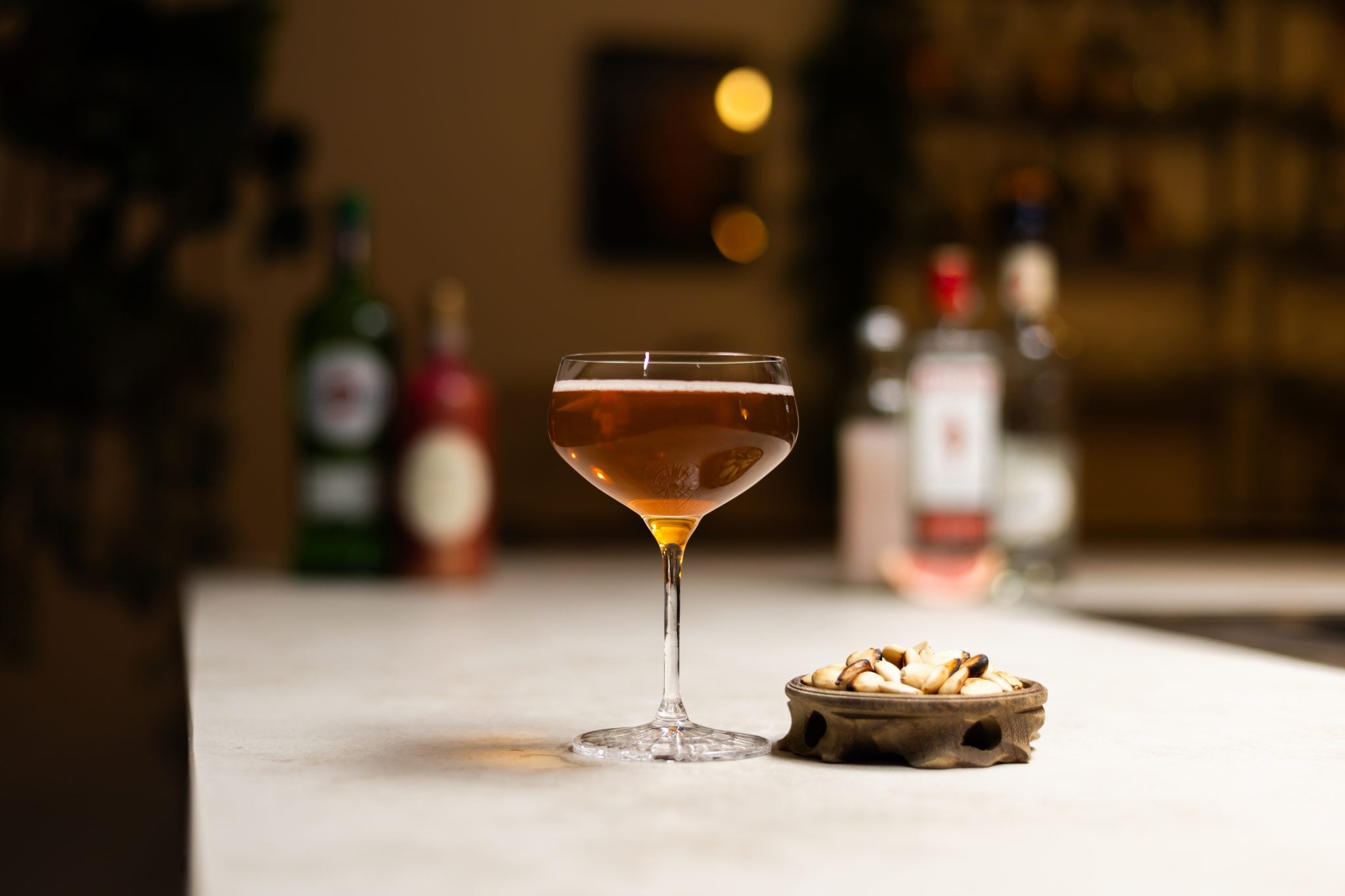 Maraschino liqueur, pink grapefruit juice, sweet vermouth, dry vermouth, london dry gin and roasted and salted almonds laid out on a white bar table