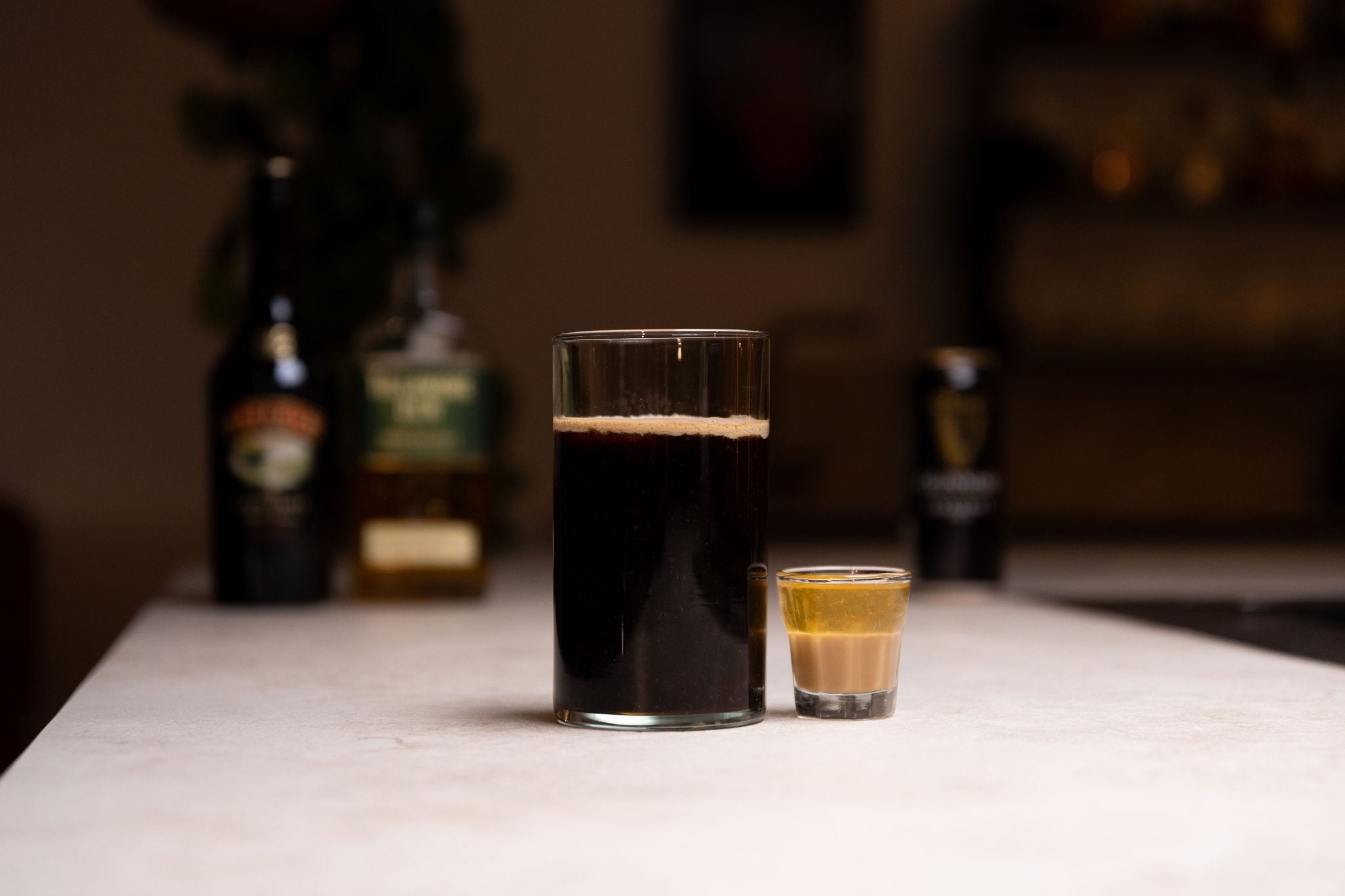 Pint Guinness, Irish cream liqueur, and Irish whiskey laid out on a white bar table