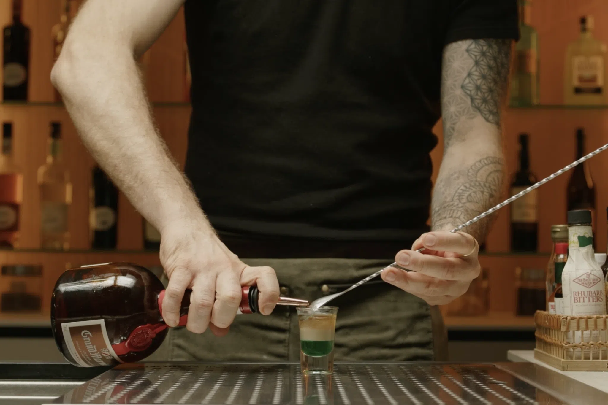 <p>For the final layer, clean the pourer and put it on the bottle of Grand Marnier. Using the same technique with the bar spoon, slowly pour the Grand Marnier over the Irish cream to create the top layer, which should fill the remaining third of the glass. The three layers—green crème de menthe, white Irish cream, and orange Grand Marnier—should be clearly defined, resembling the colors of the Irish flag.</p>
