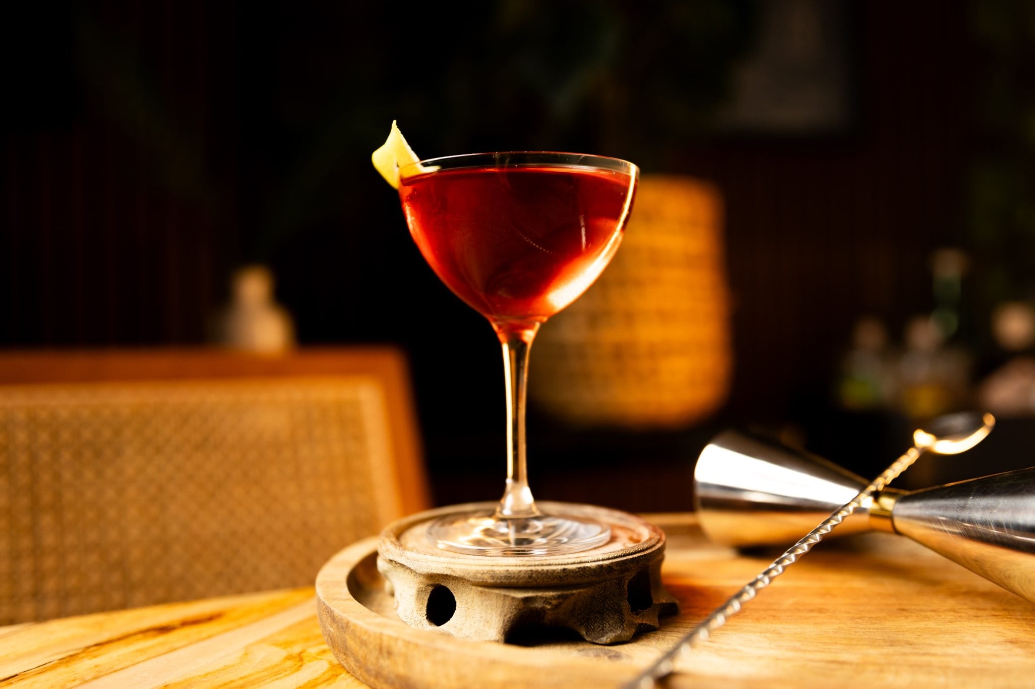 A side shot of an Islander cocktail in a coupe glass on a wooden coaster placed on a wooden board with a bar spoon and a jigger on the side