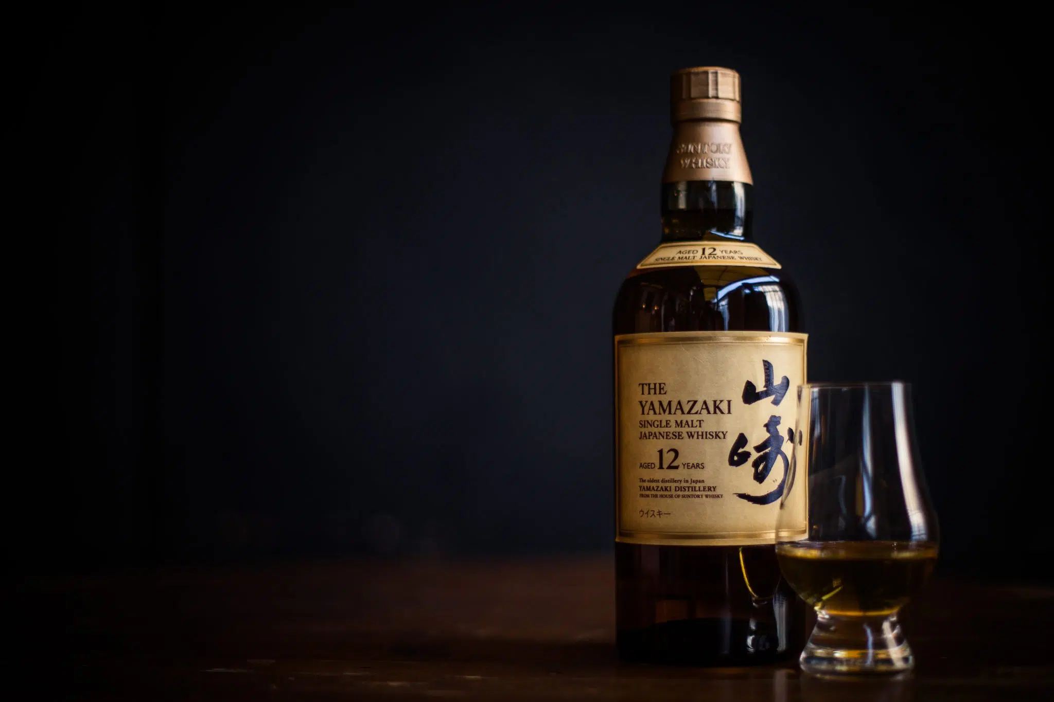A shot of a Suntory Yamazaki Japanese Whiskey bottle with a coupe glas on the side on a dark background