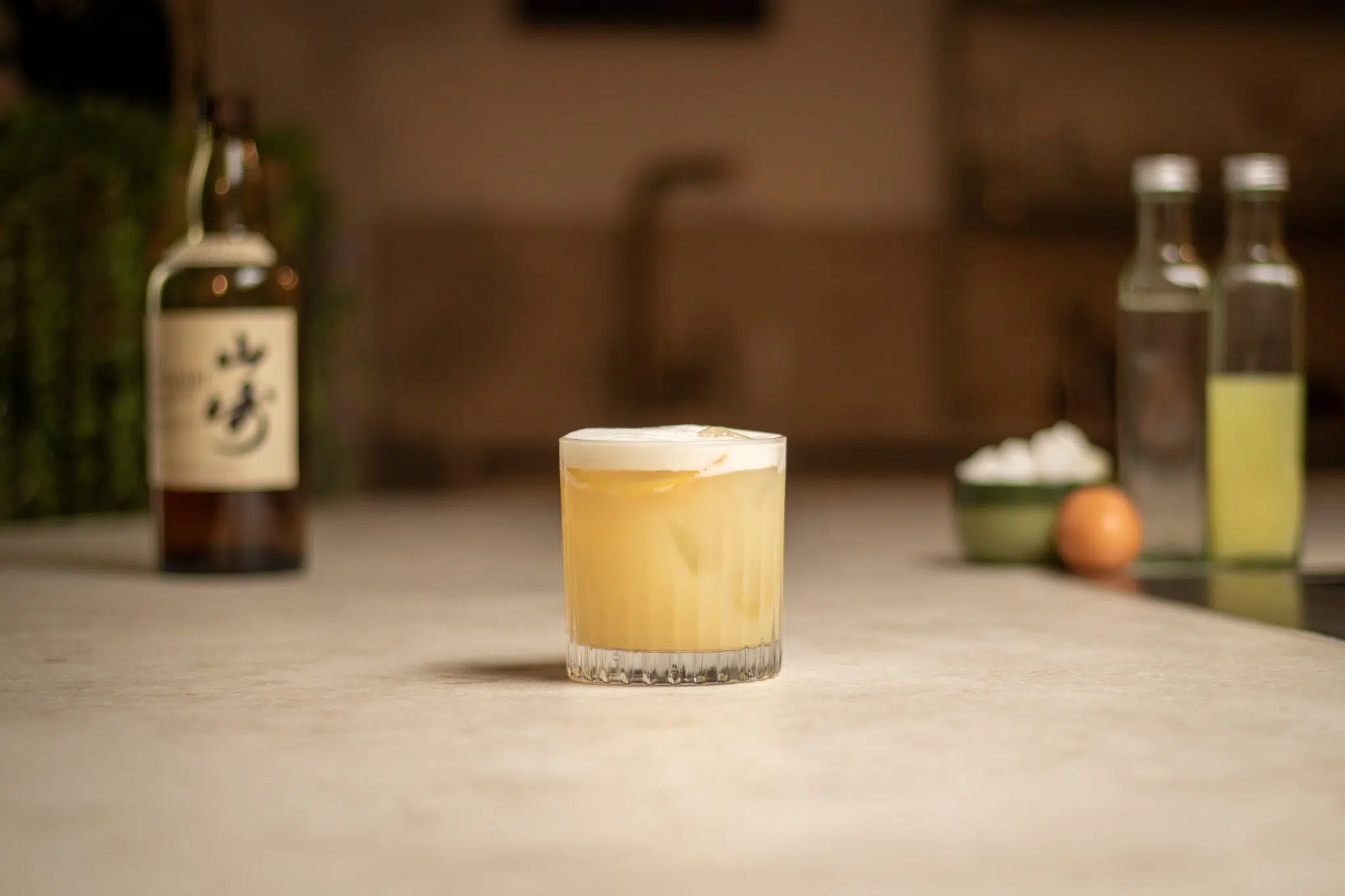 Yuzu Whisky, yuzu juice, simple syrup, sugar cubes in a green bowl and egg laid out on a white bar table