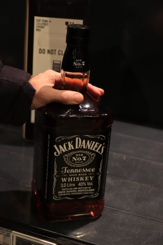 A shot of a hand holding a 3 liters bottle of a Jack Daniel's on a grey surface