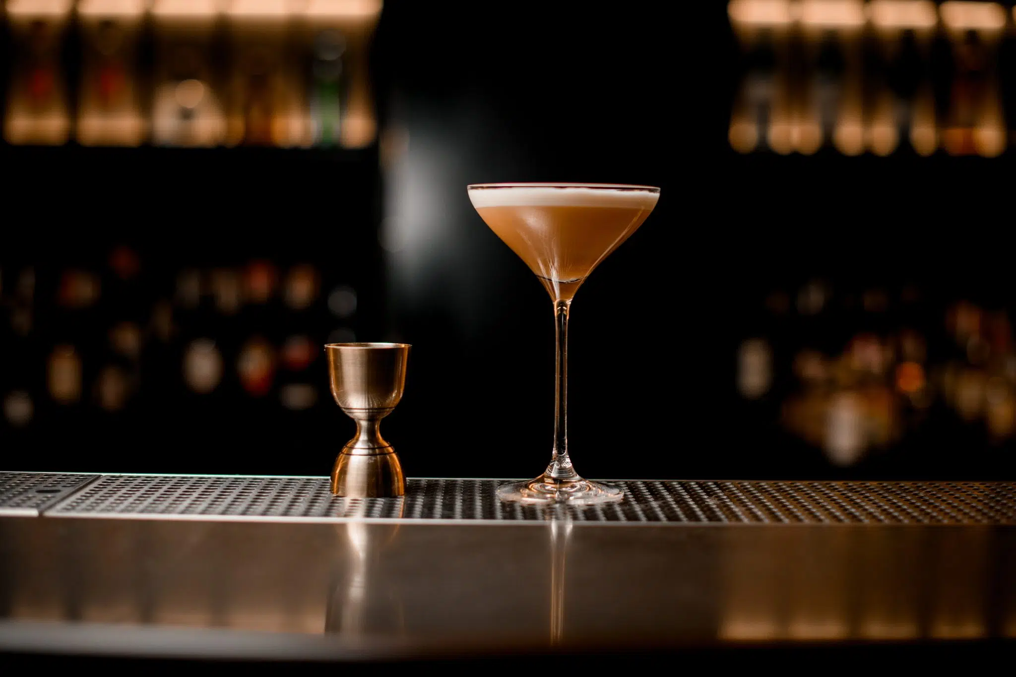 A shot of a cocktail in a martini glass and a bell jigger on a bar table