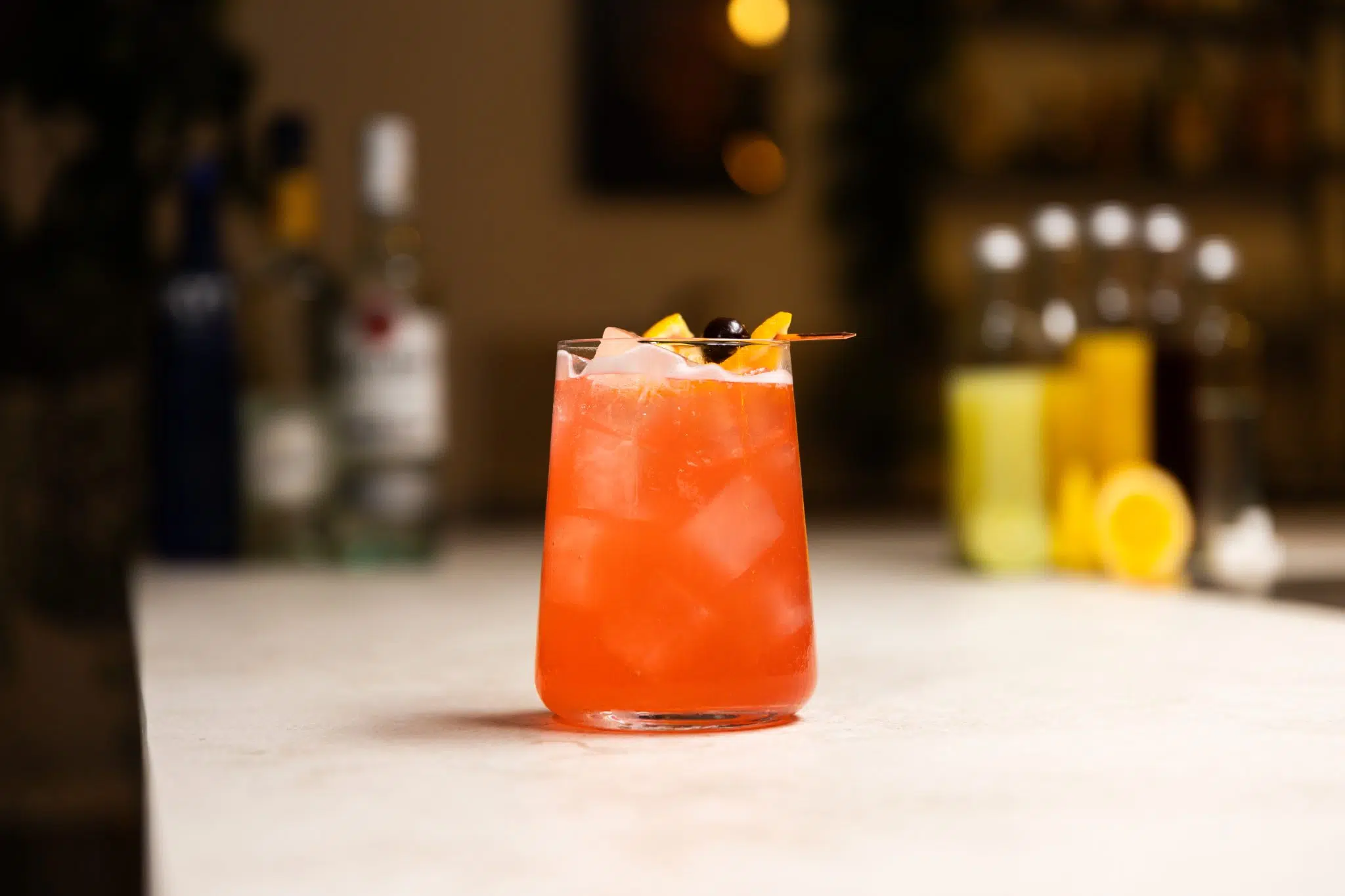 Vodka, light rum, triple sec, orange juice, orange, cranberry juice, pineapple juice, pineapple, lime juice, lime, and simple syrup laid out on a white bar table