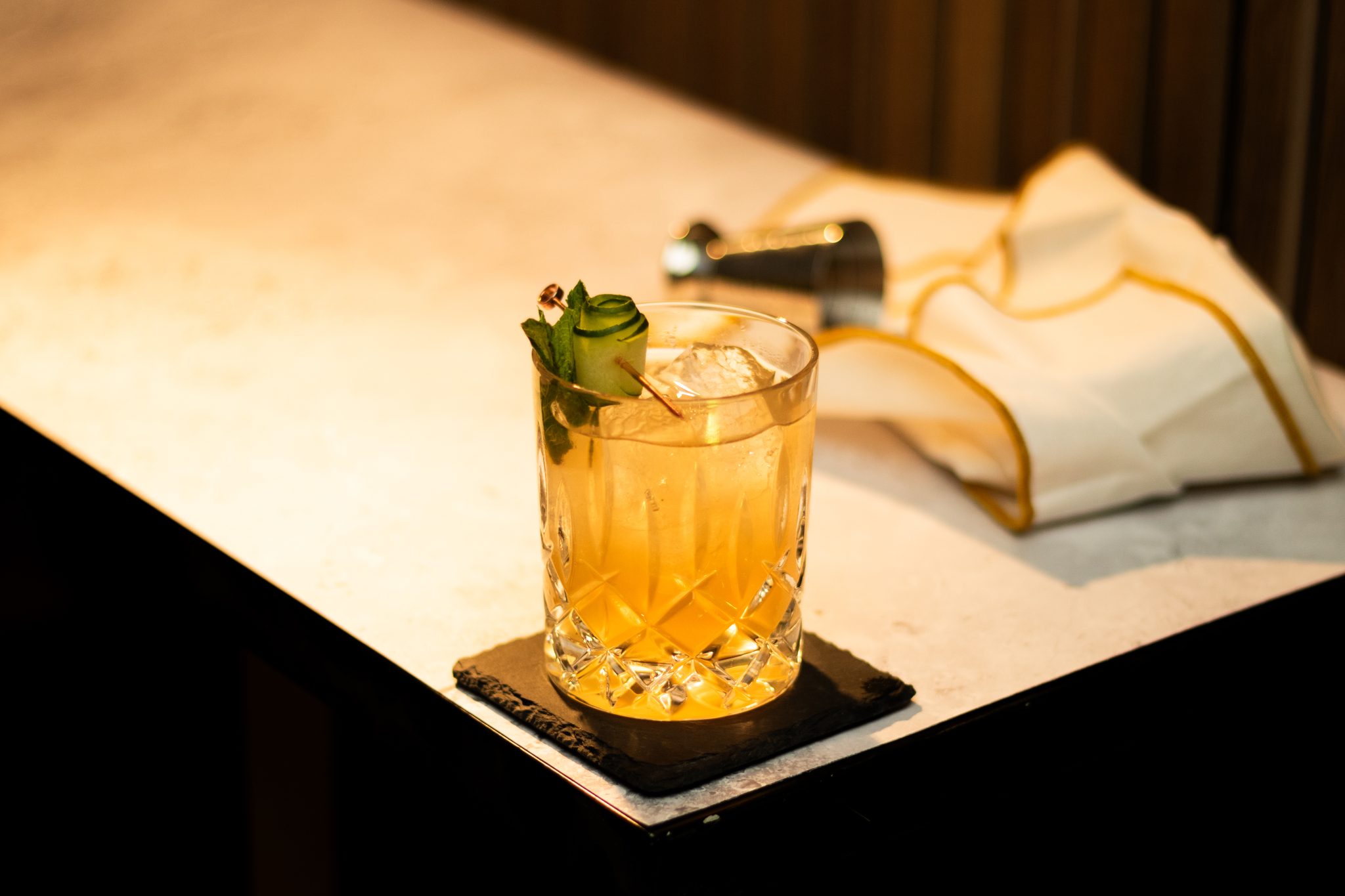 A side shot of a Kentucky Maid cocktail in an old fashioned glass on a black stone coaster placed on a white table with a white cloth and a jigger around