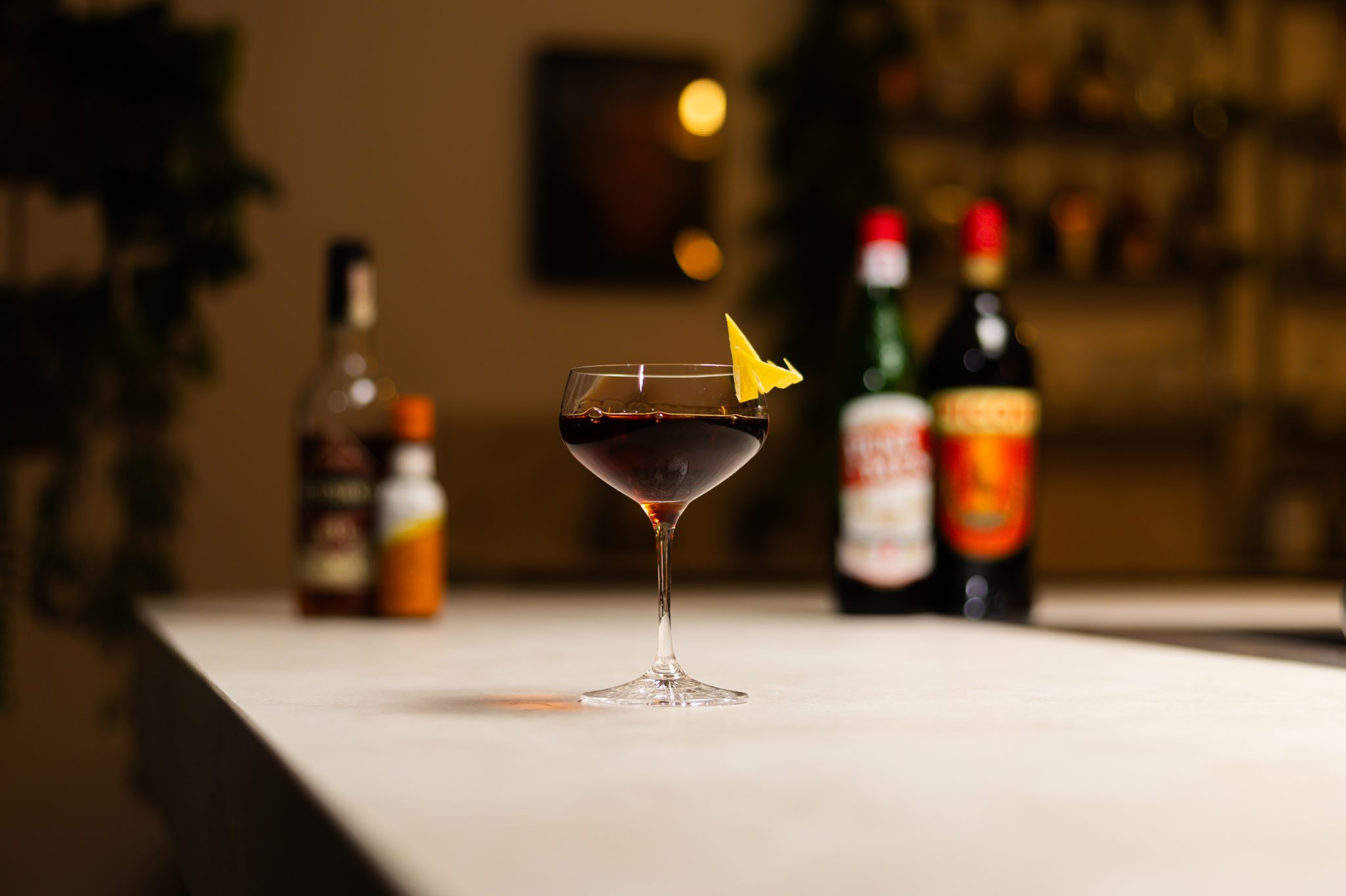 Rye Whiskey, sweet vermouth, Amer Picon, and orange bitters laid out on a white bar table