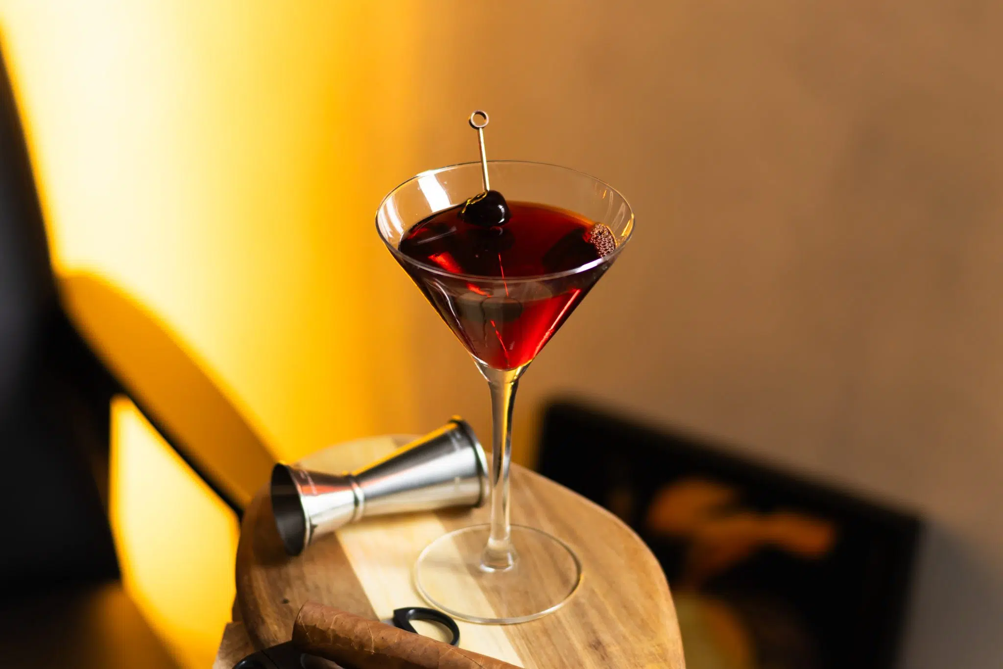 A side shot of a Little Italy cocktail in a martini glass on a wooden board with a jigger on the side