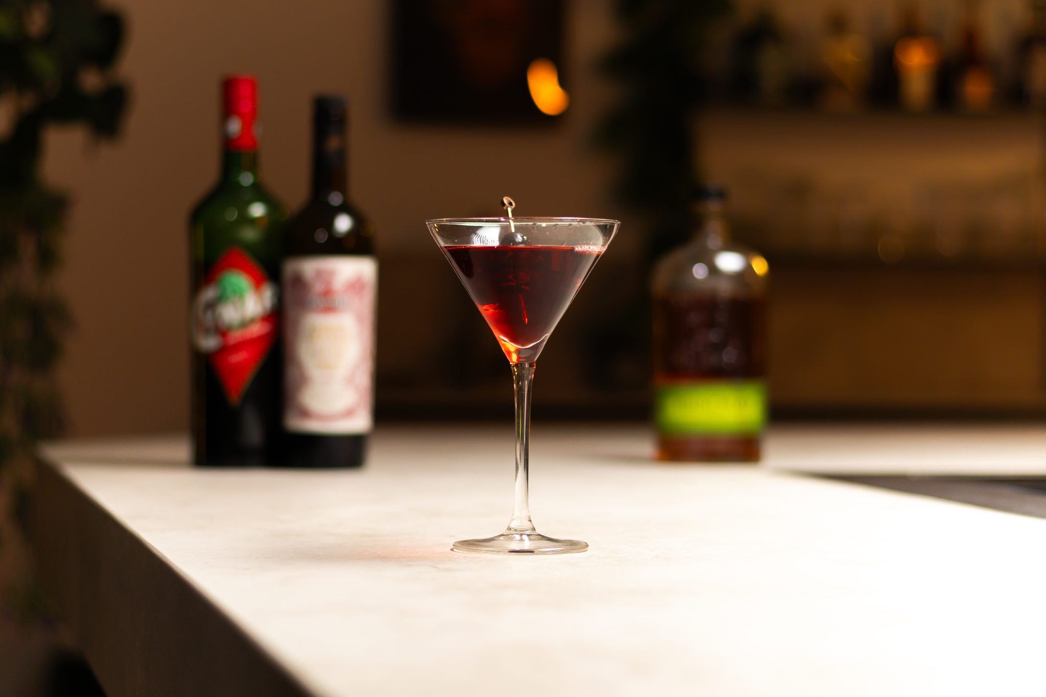 Rye whiskey, sweet vermouth and cynar laid out on a white bar table