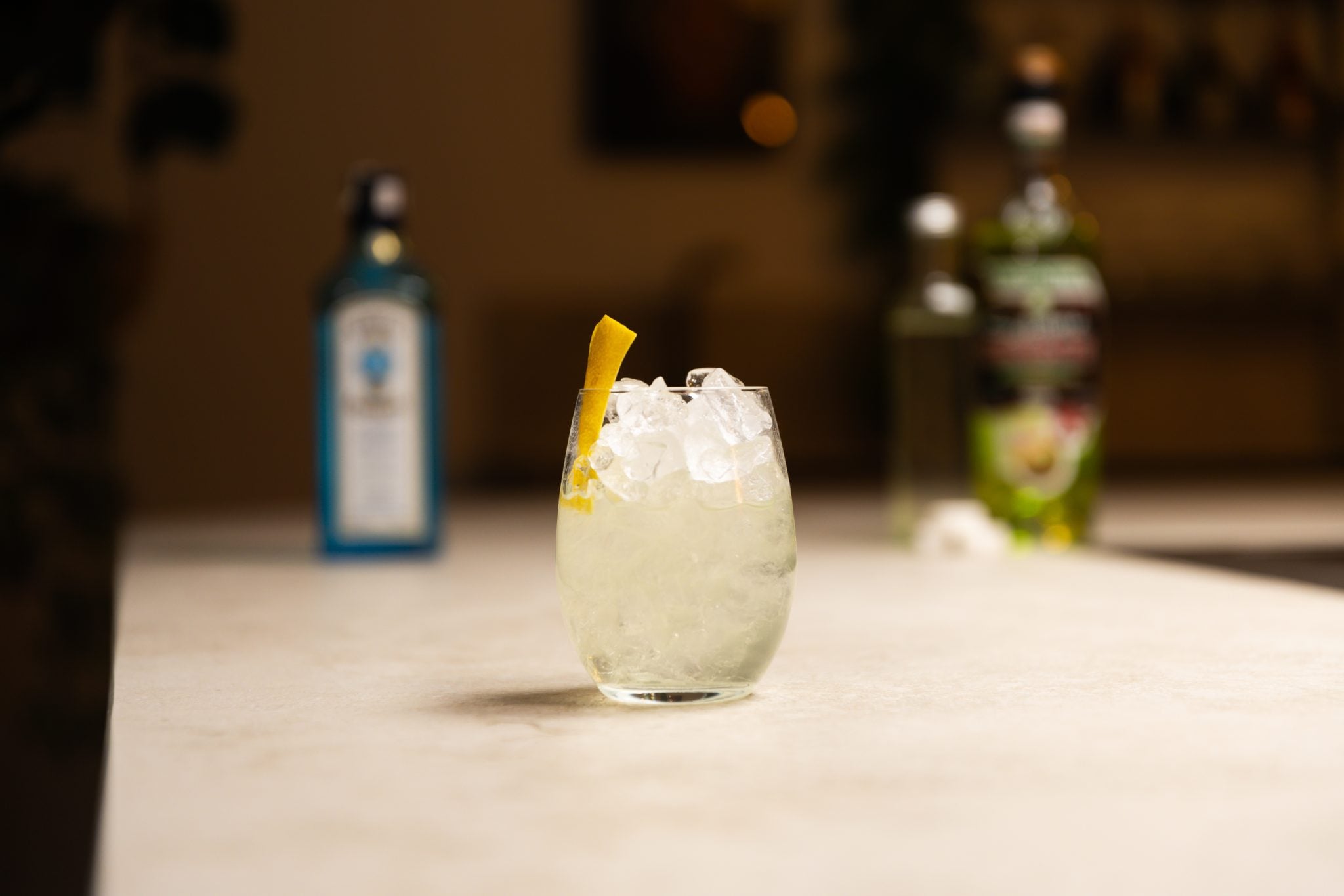 Gin, Absinthe, simple syrup, and sugar cubes laid out on a white bar table