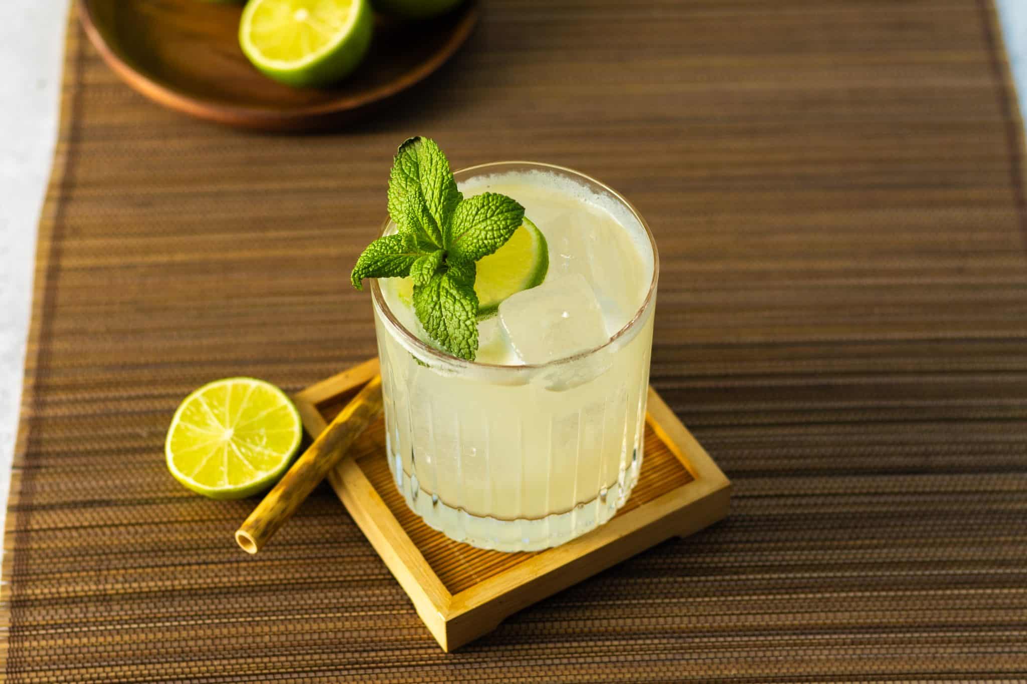 A Mai Tai cocktail, shot from above, in a rocks glass on a wooden coaster placed on a brown placemat with a cinnamon stick and a lime wheel on a side.