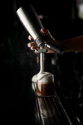 A shot of a whipping siphon making foam on a coffee cocktail