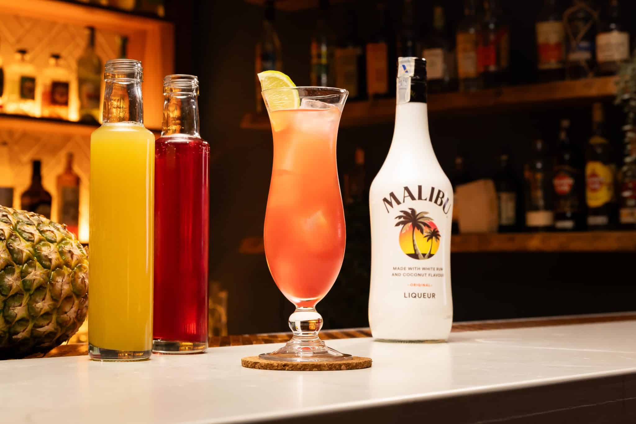 Malibu Coconut rum, cranberry juice and pineapple juice laid out on a white bar table