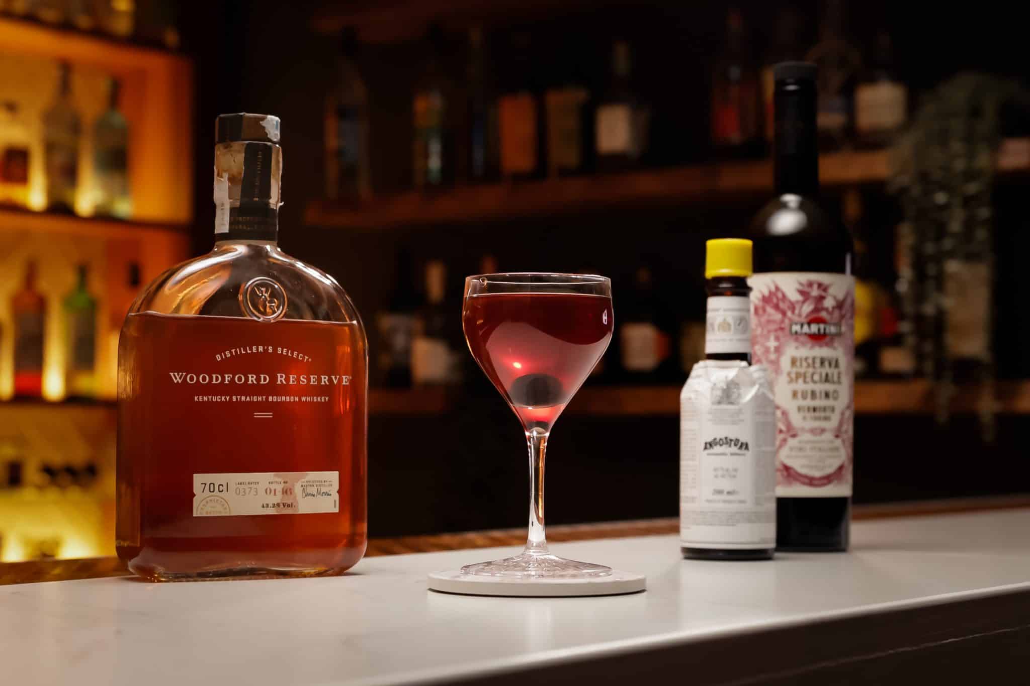 Rye whiskey, sweet vermouth and Angostura bitters laid out on a white bar table