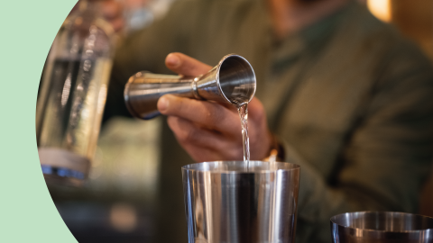 A shot of a person pouring simple syrup with a jigger into a cocktail shaker