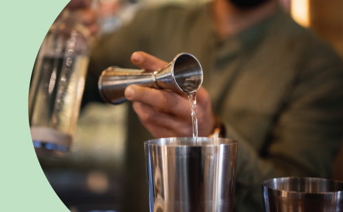 A shot of a person pouring simple syrup with a jigger into a cocktail shaker