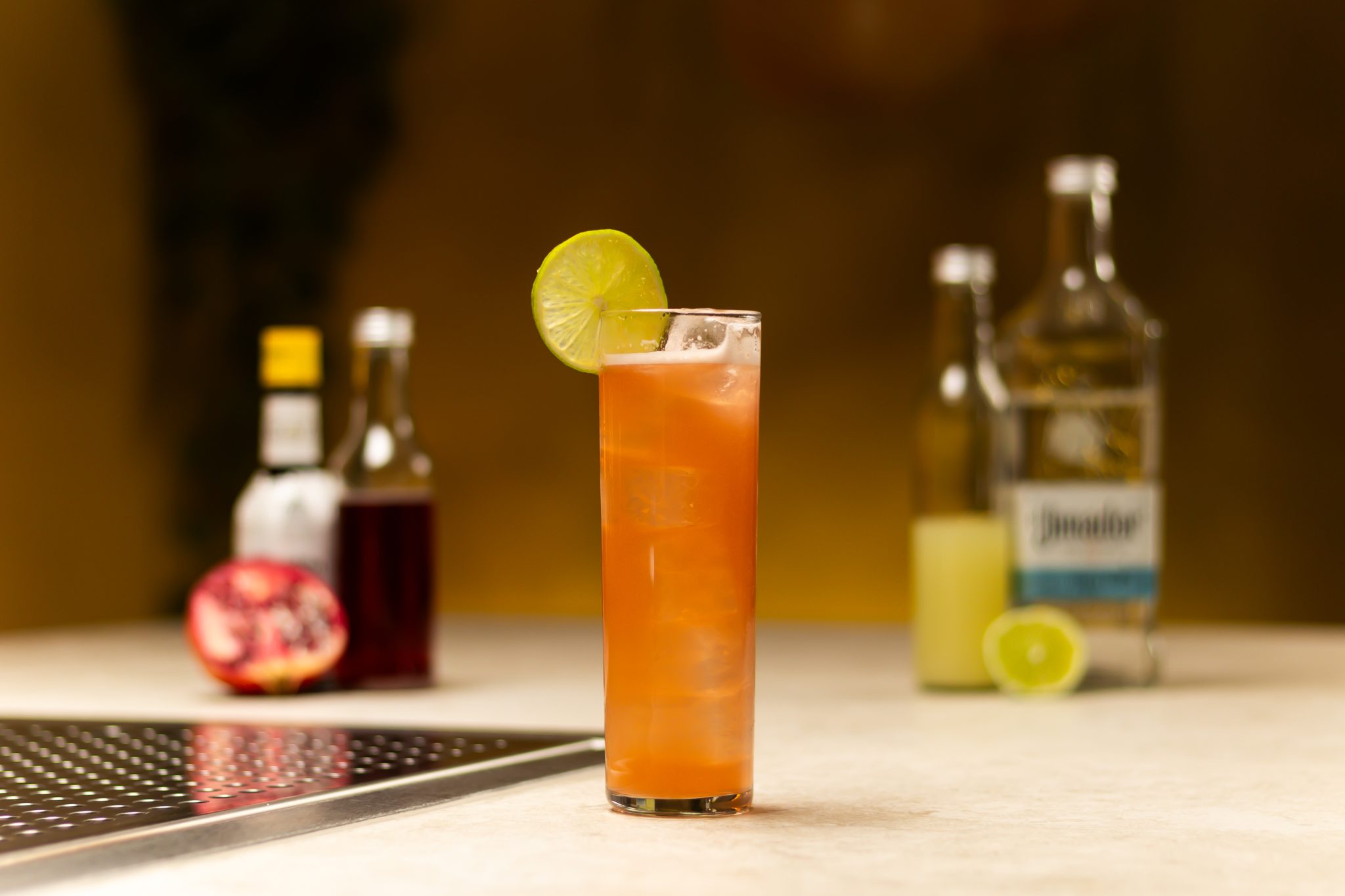 Tequila, lime juice, grenadine, Angostura aromatic bitters, pomegranate and lime laid out on a white bar table