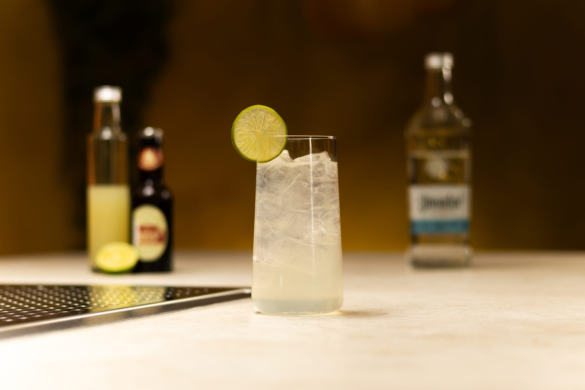 Tequila, ginger beer, lime juice and lime laid out on a white bar table