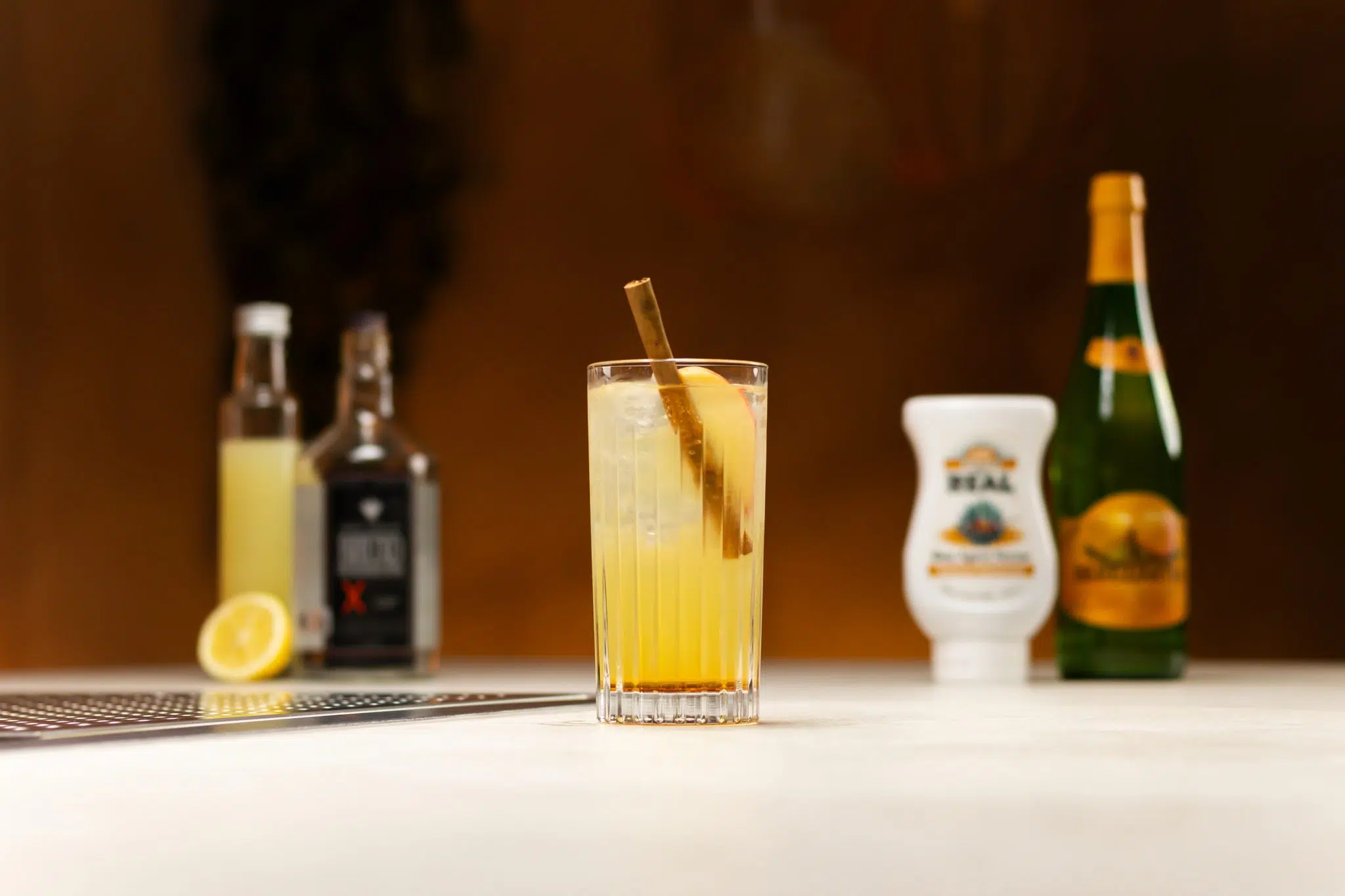 Apple Cider, Mezcal, agave syrup, lemon juice and lemon laid out on a white bar table