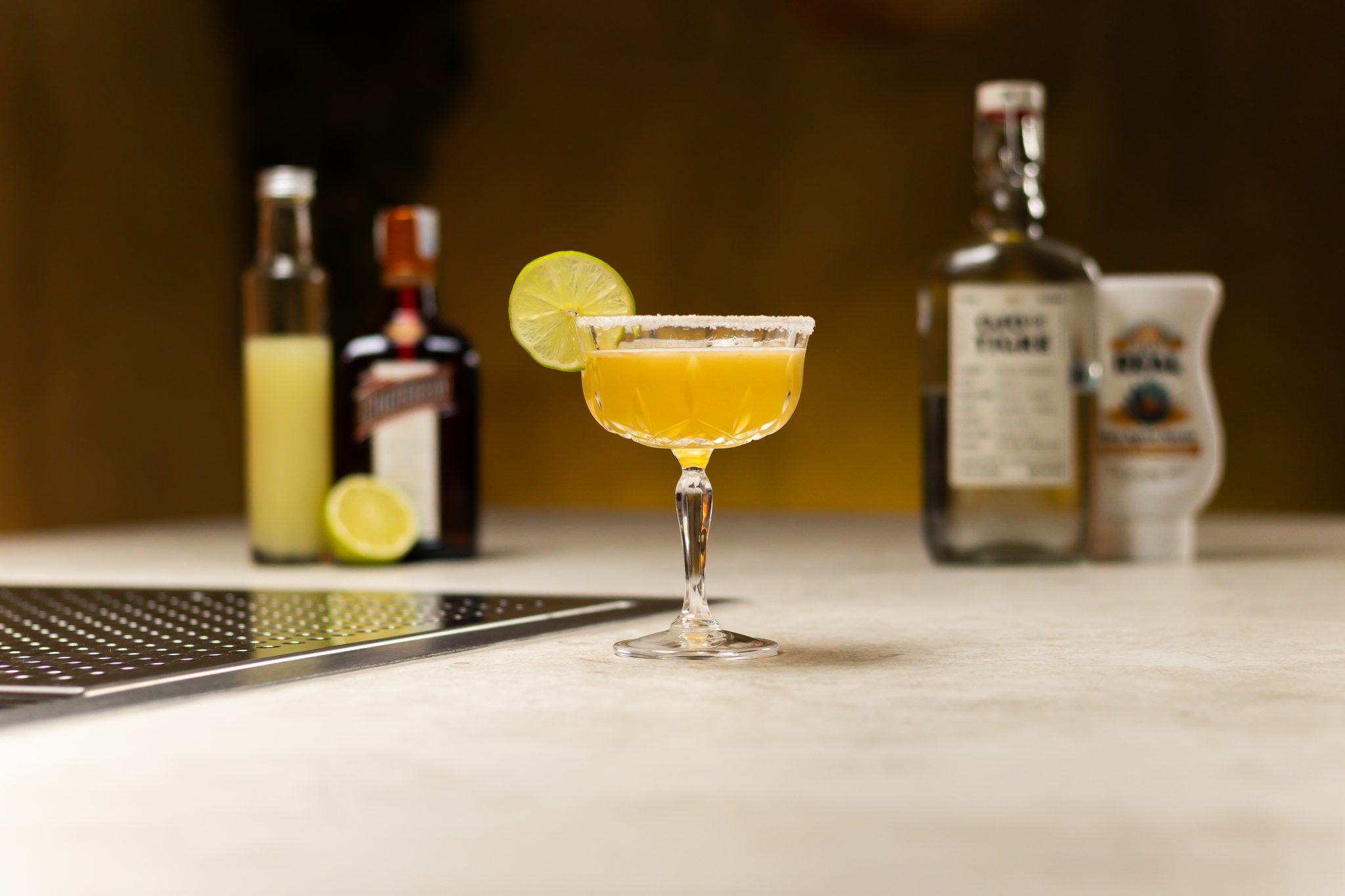 Mezcal, orange liqueur, lime juice, agave syrup, and lime laid out on a white bar table