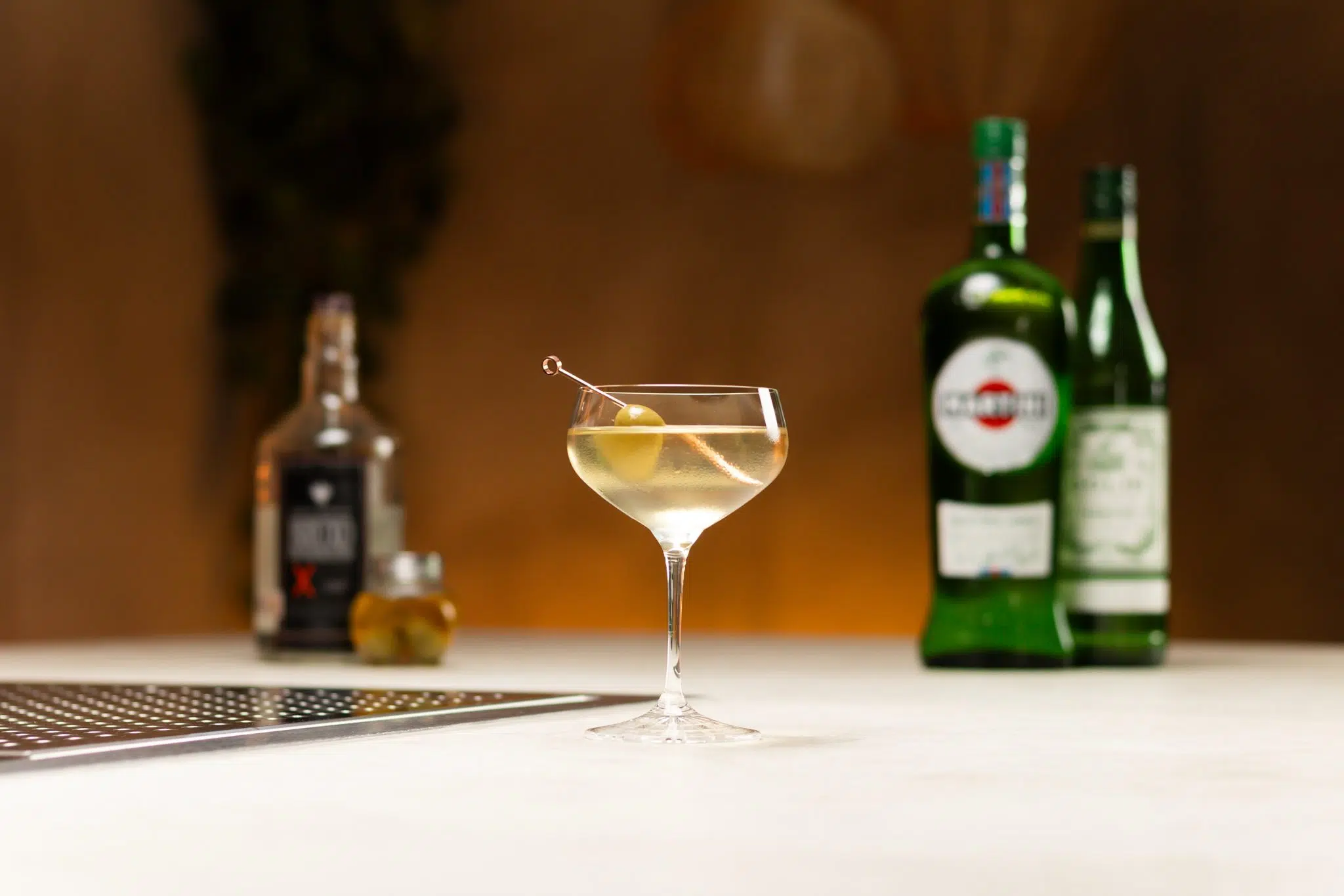 Espadin Mezcal, dry Vermouth, extra dry Vermouth, olive and olive brine laid out on a white bar table