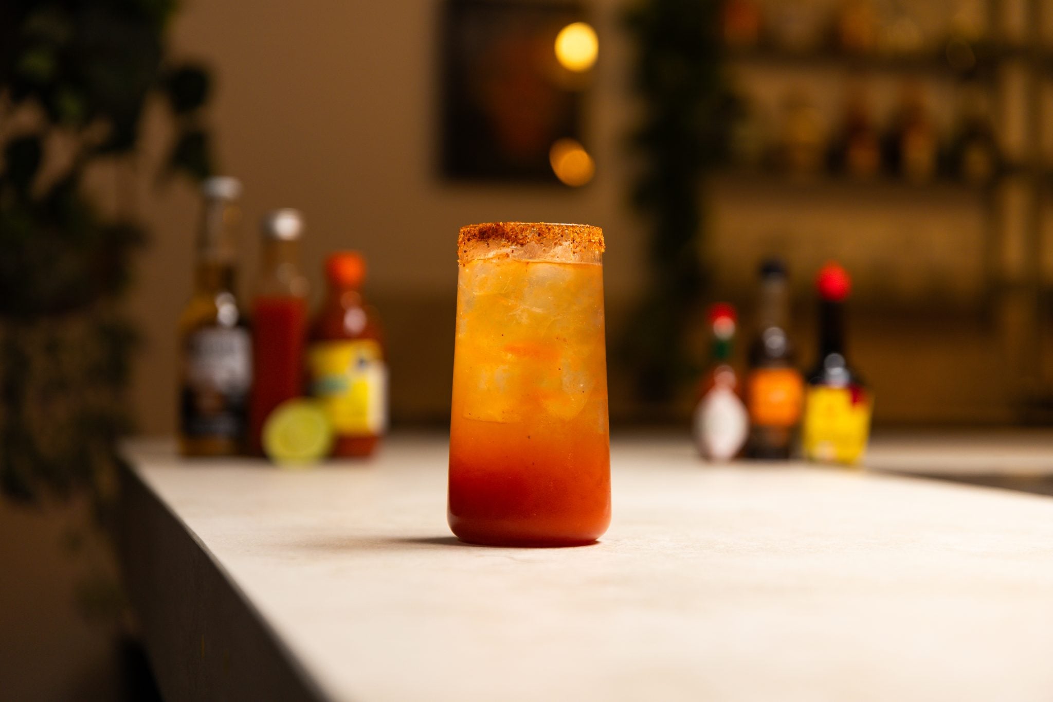 Valentina sauce, Tabasco, light beer, lime juice, lime, Maggi sauce, tomato juice, and Worcestershire sauce laid out on a white bar table