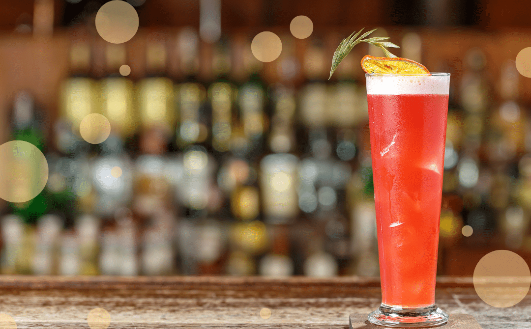 A vibrant red drink garnished with an orange wheel, elegantly positioned on a bar coaster.
