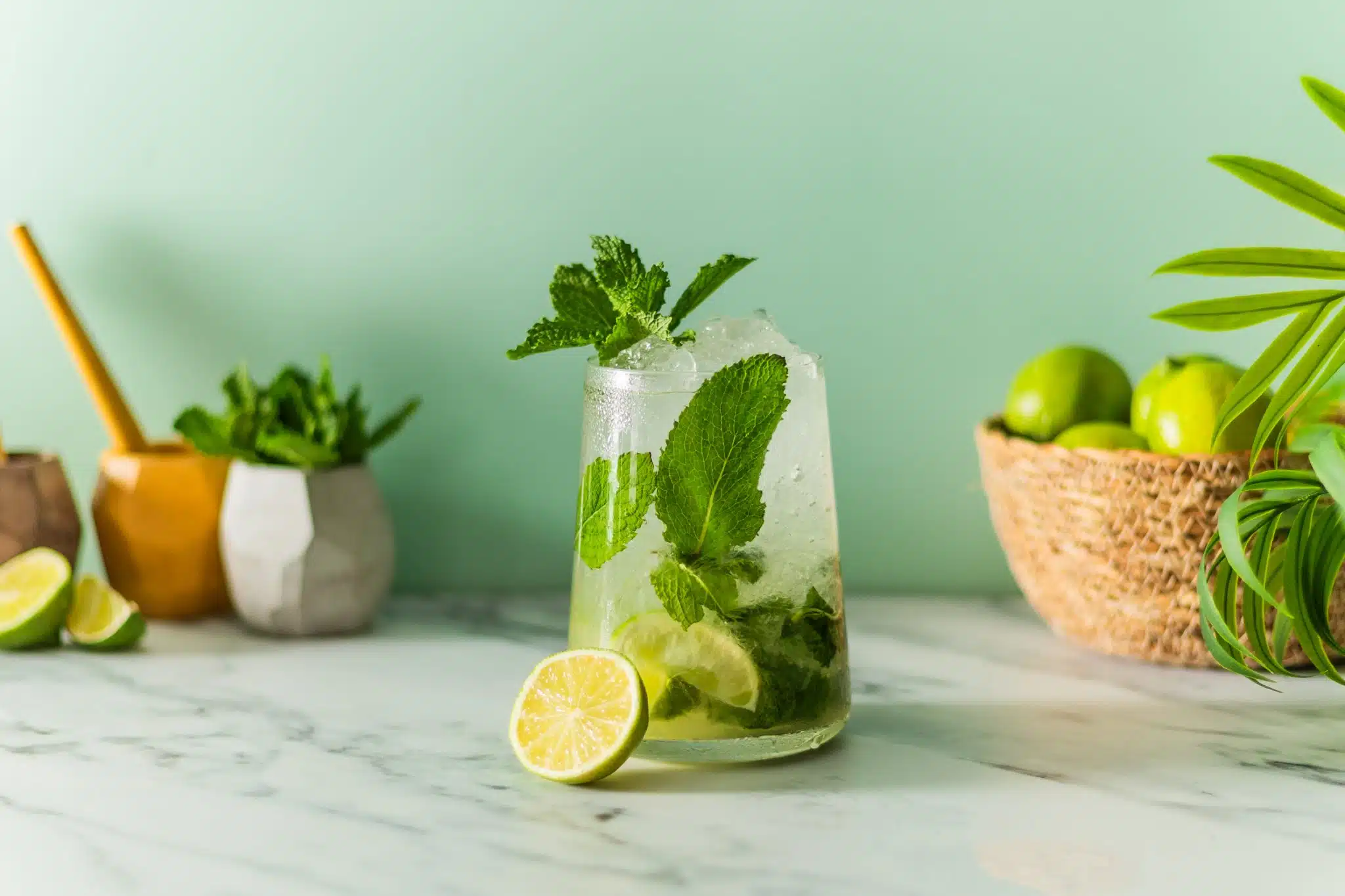 A side shot of a Mojito cocktail in a highball glass on a white marmol table with half of a lime on the side