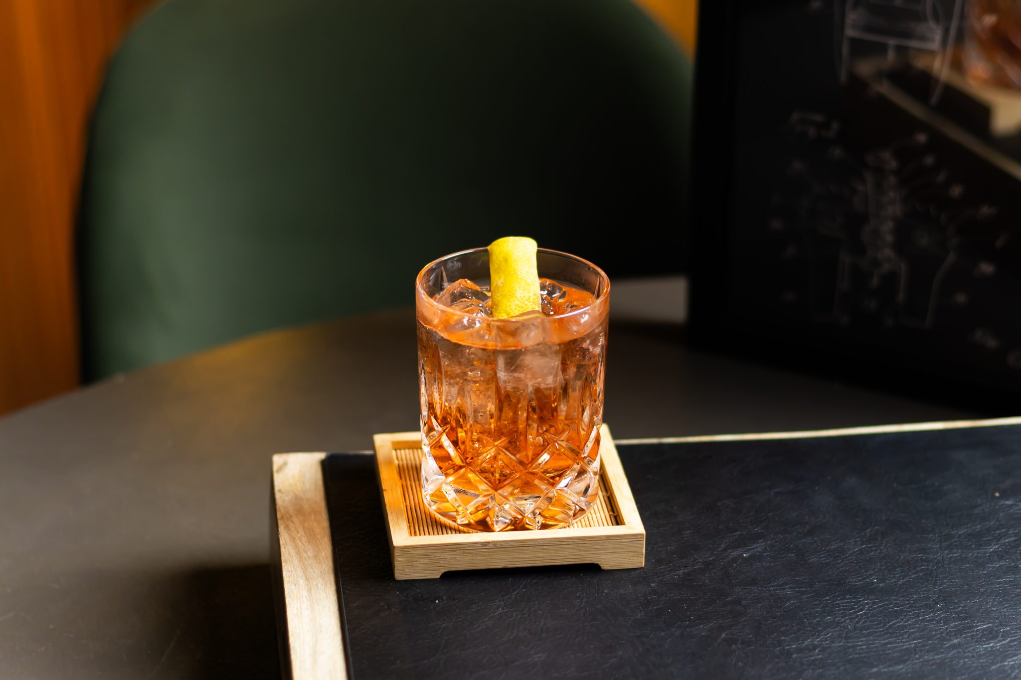 A side shot of a Monte Carlo cocktail in an old fashioned glass on a wooden coaster placed on a black surface