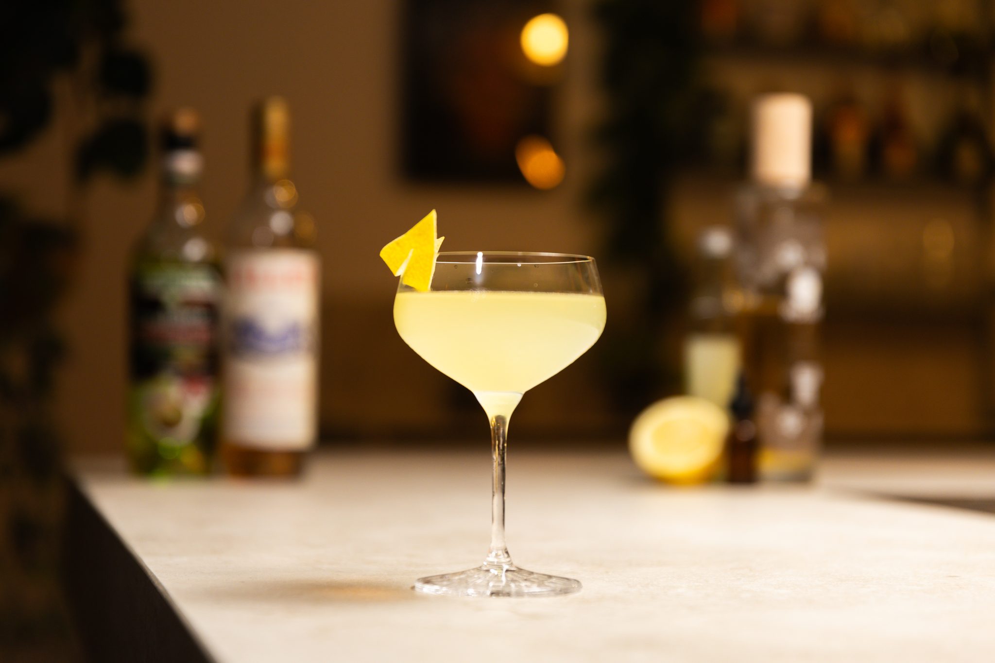 Absinthe, Gin, Lillet Blanc, eldderflower liqueur, lemon juice and lemon laid out on a white bar table