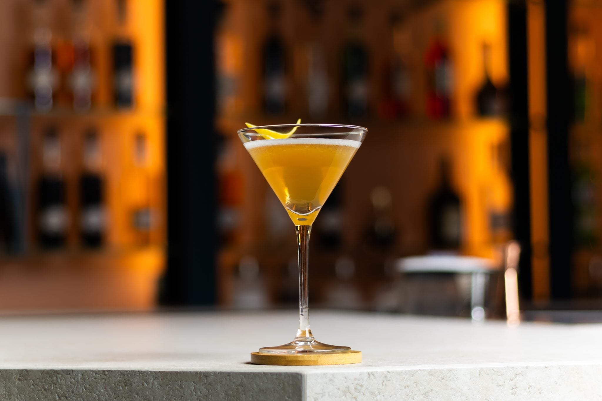 A side shot of a New York cocktail in a martini glass on a wooden coaster placed on a white bar table