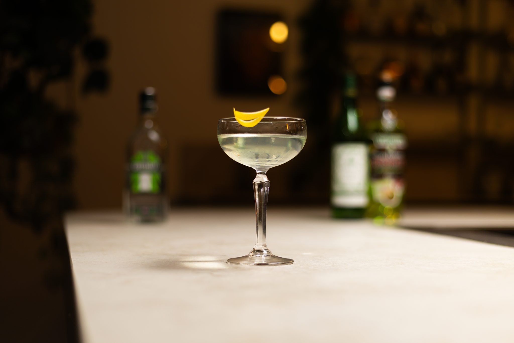 Gin, Absinthe and Dry Vermouth laid out on a white bar table
