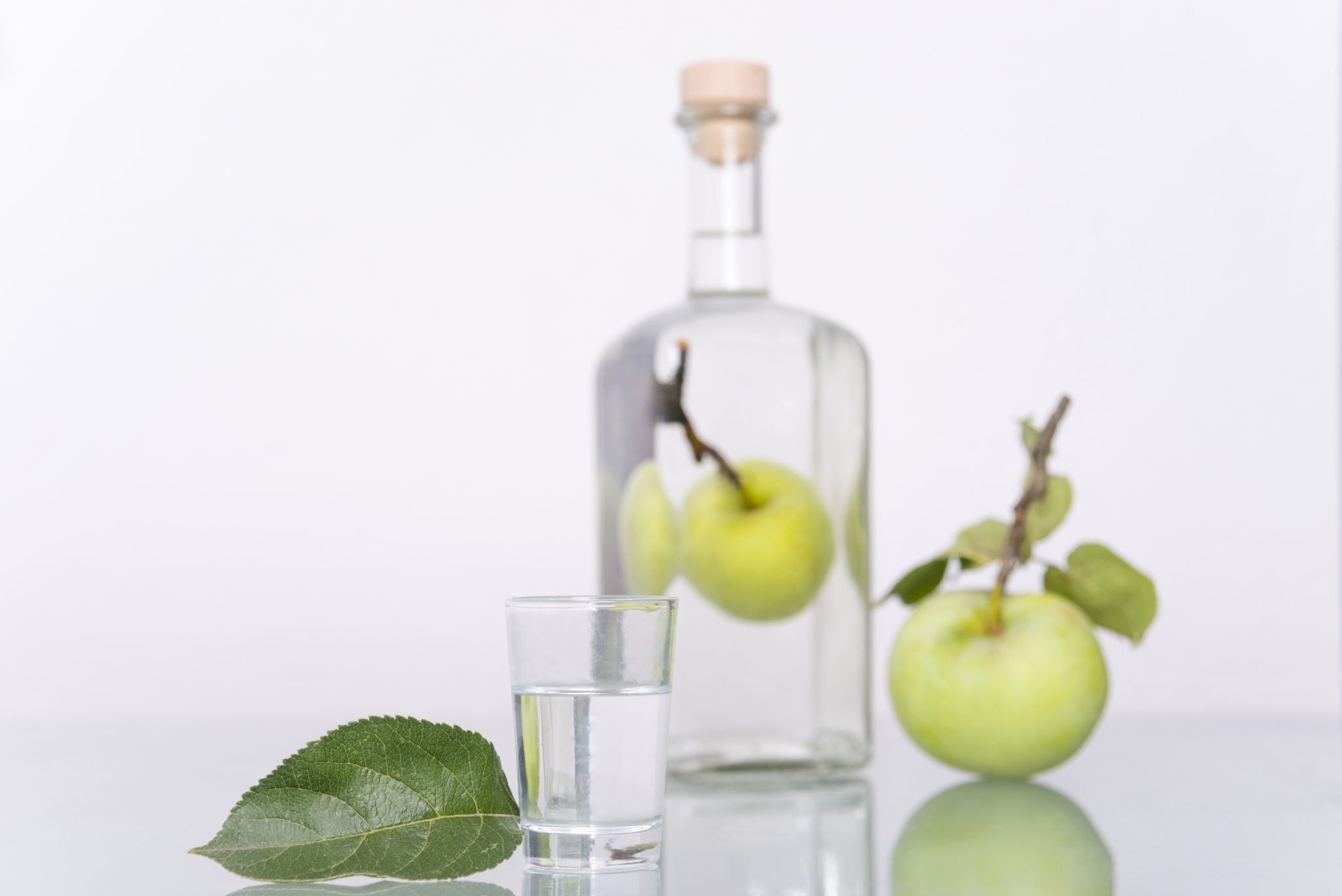 A Obstlet shot with an apple leave, a green apple, and a Obstler bottle with an apple inside, in front of a white background