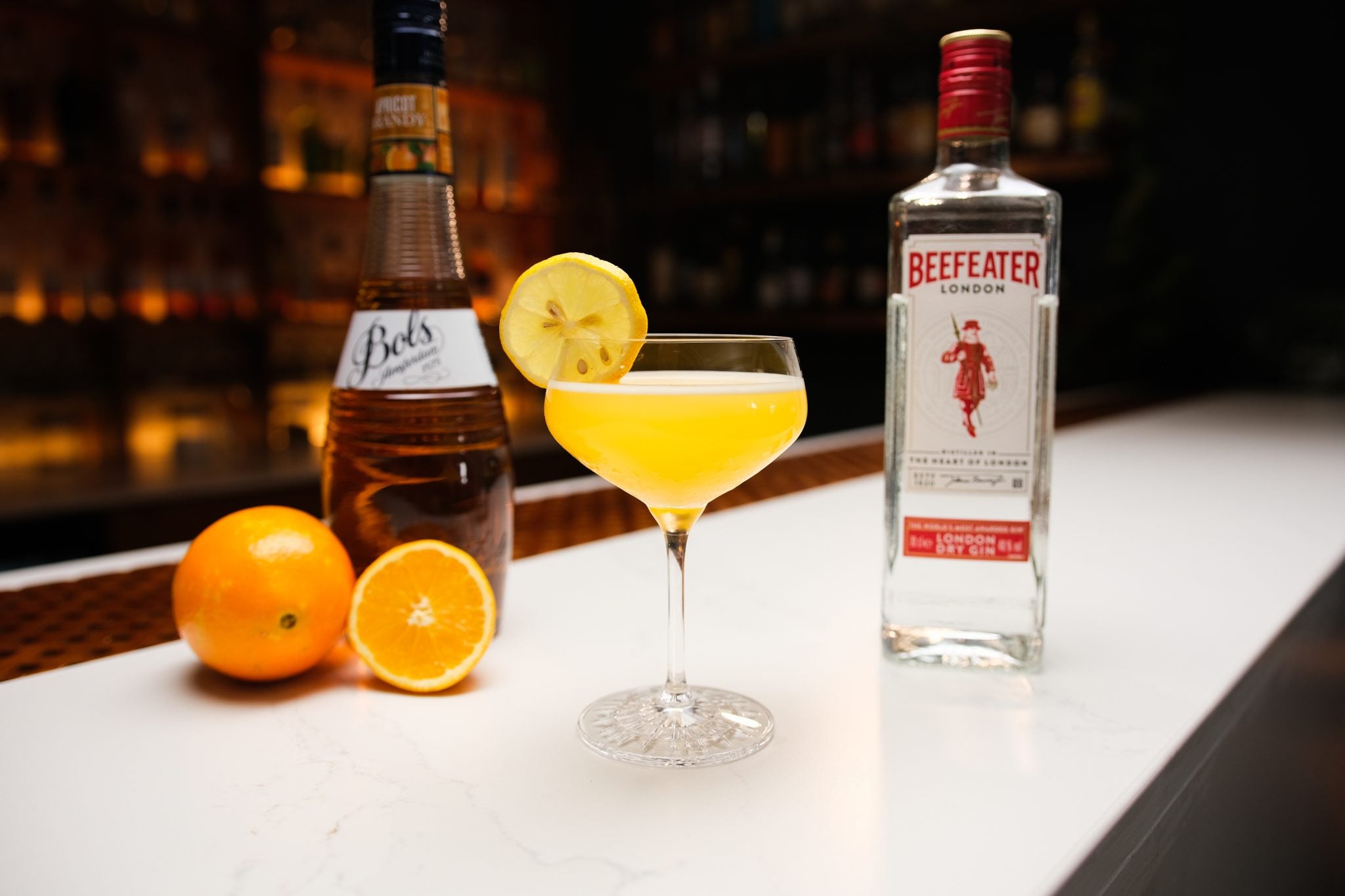 Gin, apricot Brandy, two oranges laid out on a white bar table.