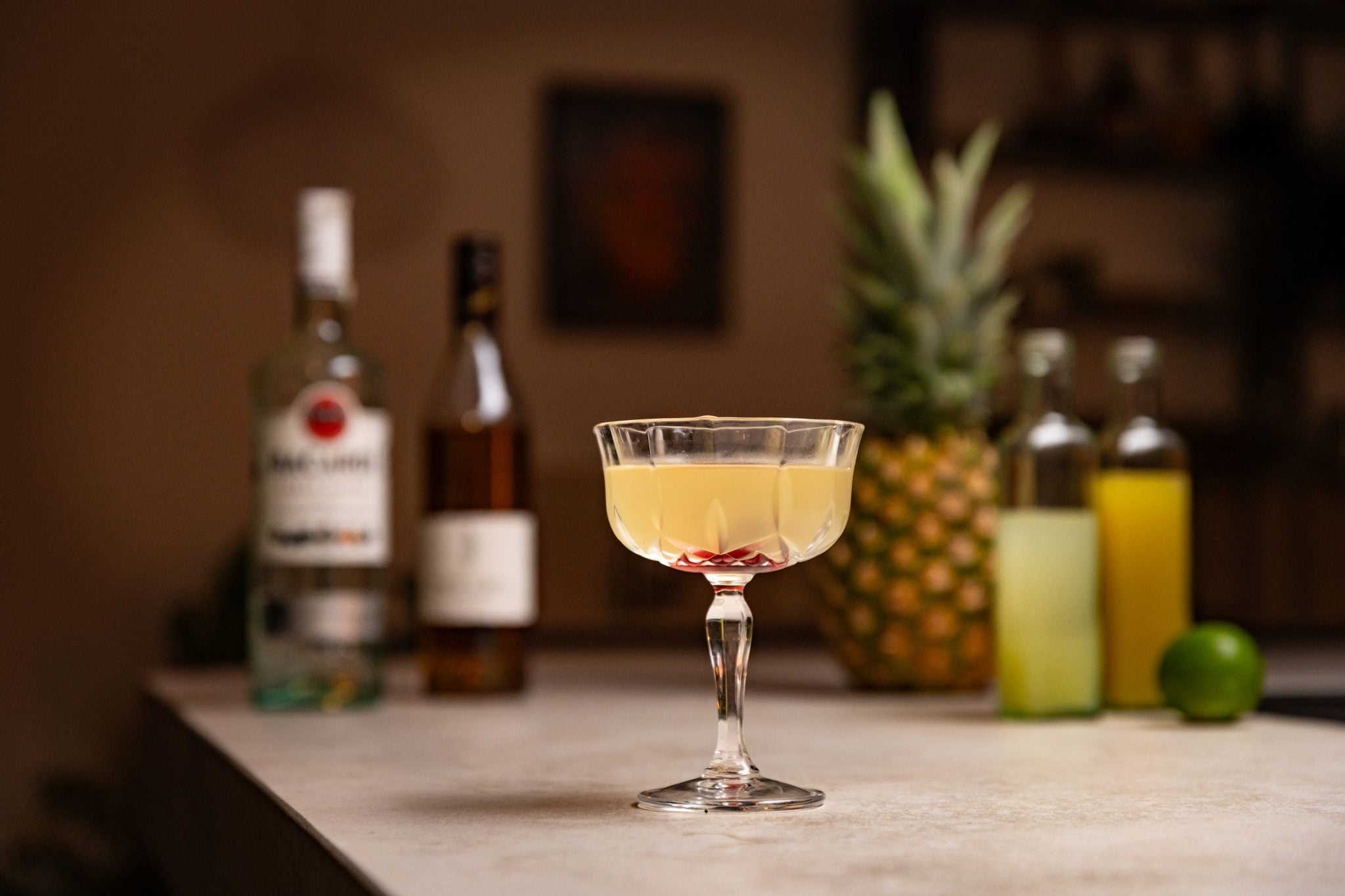 White Rum, banana liqueur, pineapple juice, pineapple, lime juice, and lime laid out on a white bar table