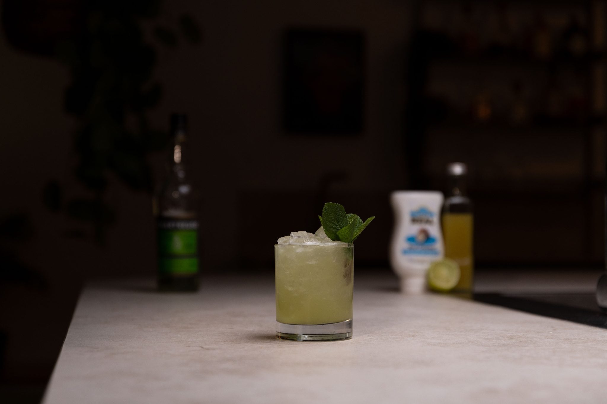 Green Chartreuse, pineapple juice, lime juice, lime, and coconut cream laid out on a white bar table