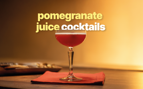 A side shot of a pomegranate cocktail in a coupe glass on a red napkin placed on a borwn surface with a brown plate behind