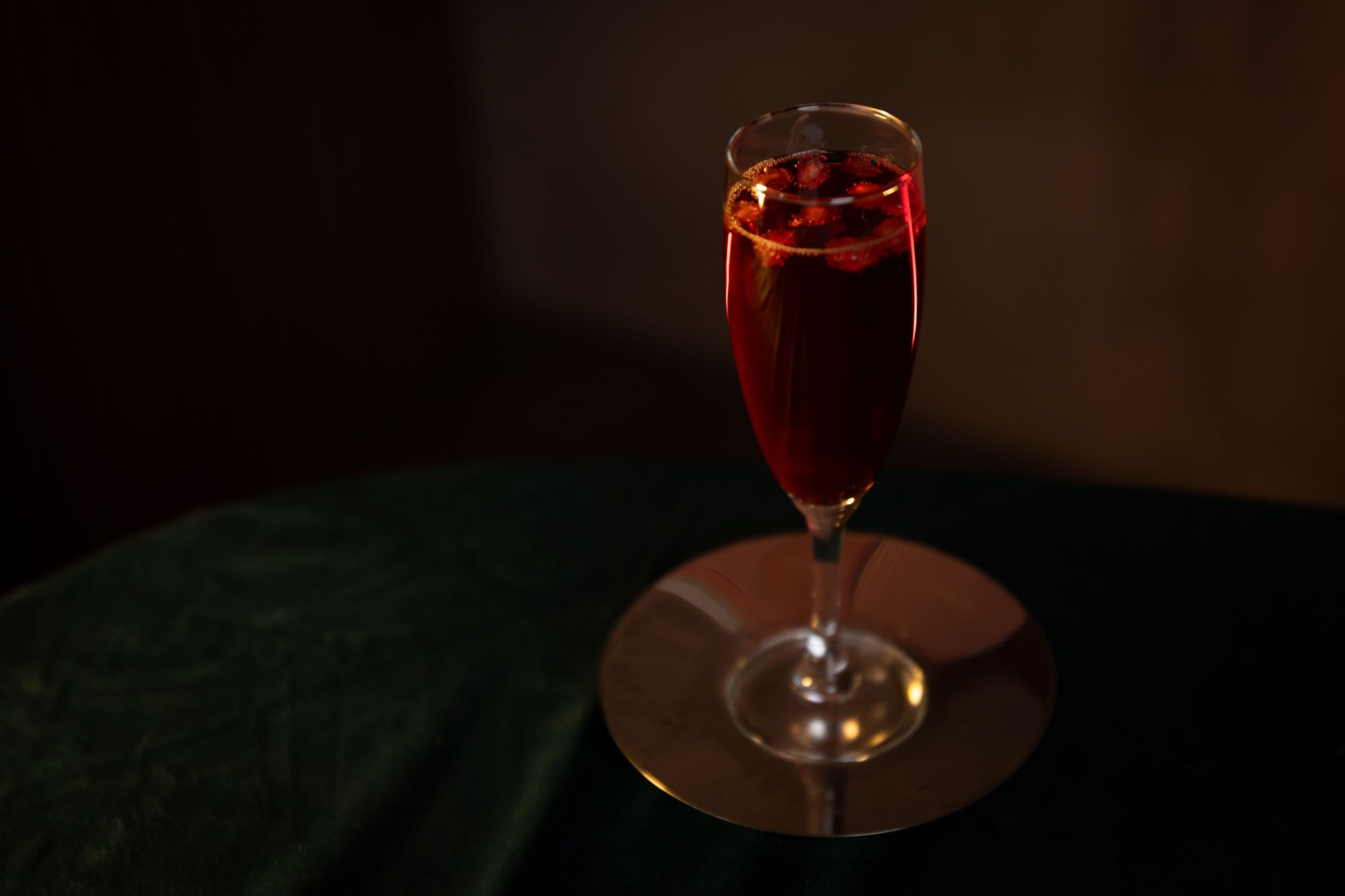 A side shot of a Pomegranate Mimosa cocktail in a champagne flute on a silver plate placed on a dark green tablecloth