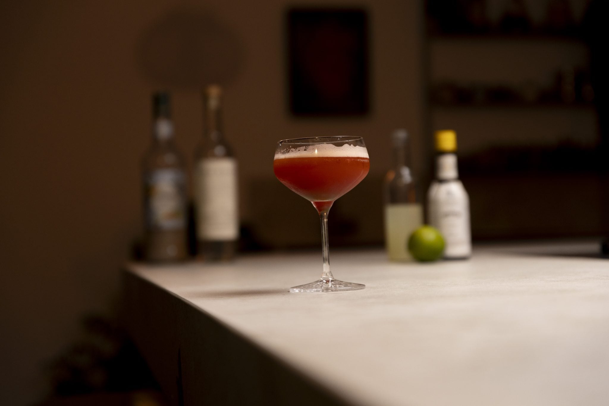 Mezcal, orgeat, lime juice, Angostura bitters, and lime laid out on a white bar table