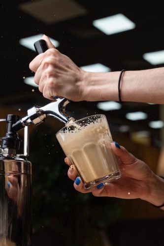 A shot of a person pouring a creamy cocktail using a tap and nitrogen