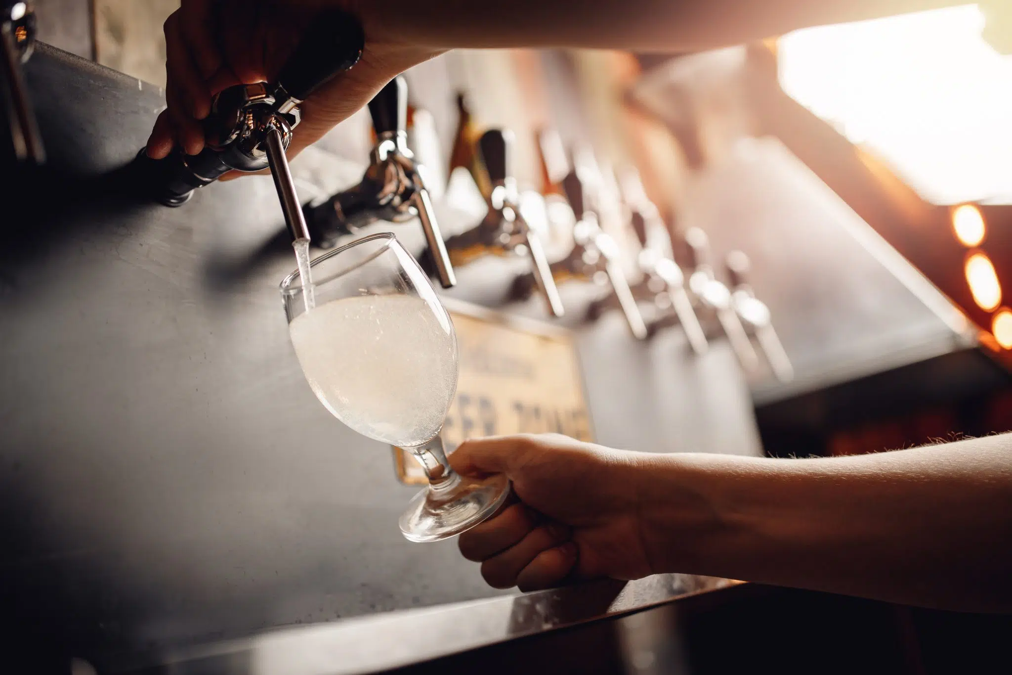 A shot of a person pouring a cloudy cocktail in a white wine glass using a tap